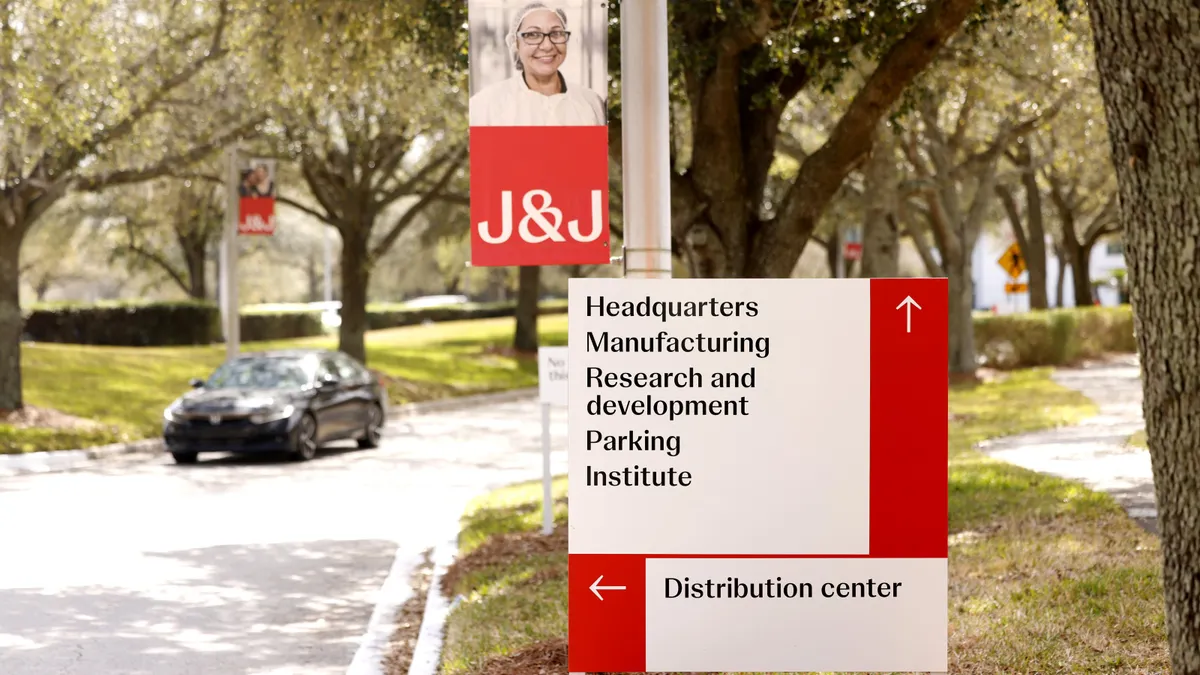 A car drives down a road lined with trees toward a sign that reads "Headquarters Manufacturing Research and development Parking Institute Distribution center."