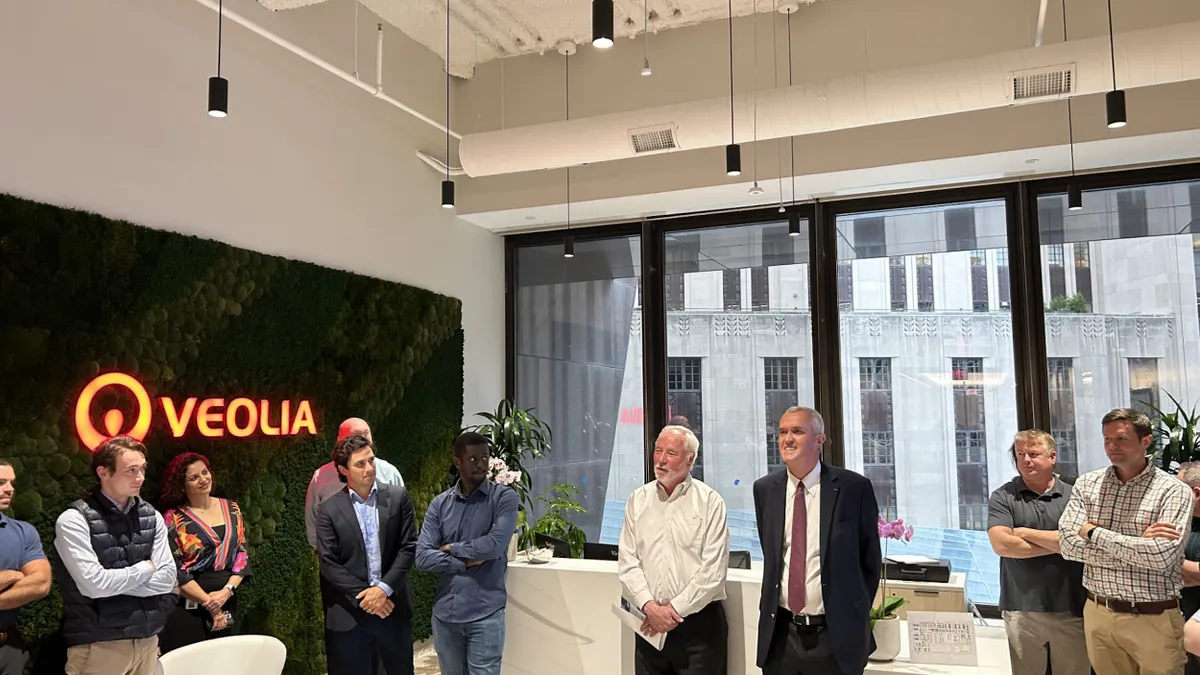 A group of people stand in a Boston office space, with the Veolia logo on a green wall to the left
