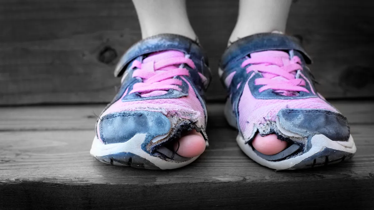 A close-up shot of shoes with holes in them, with a child's toes poking out.