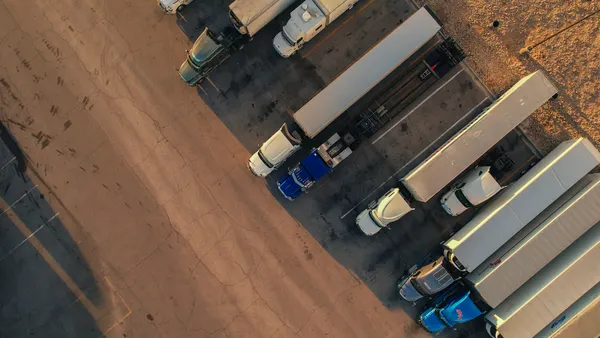 Tractors-trailers and a flatbed truck shown from an aerial drone view directly overhead at a truckstop in Texas.