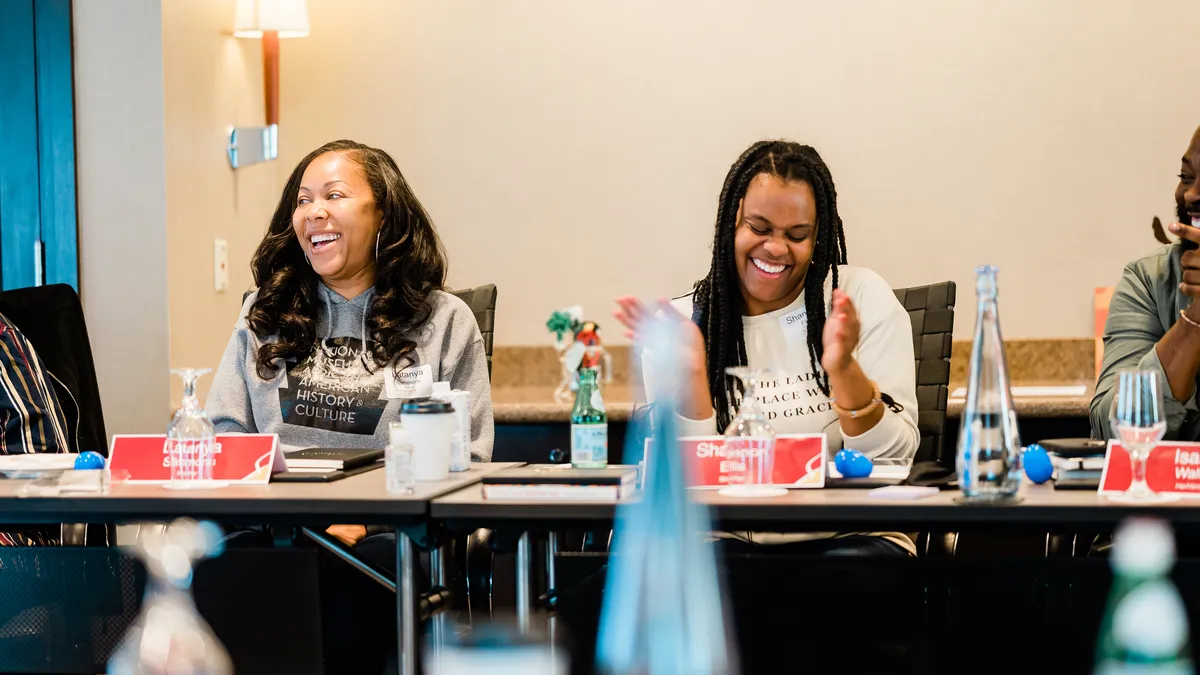 Two adults sit at a table. They are smiling and one is clapping.