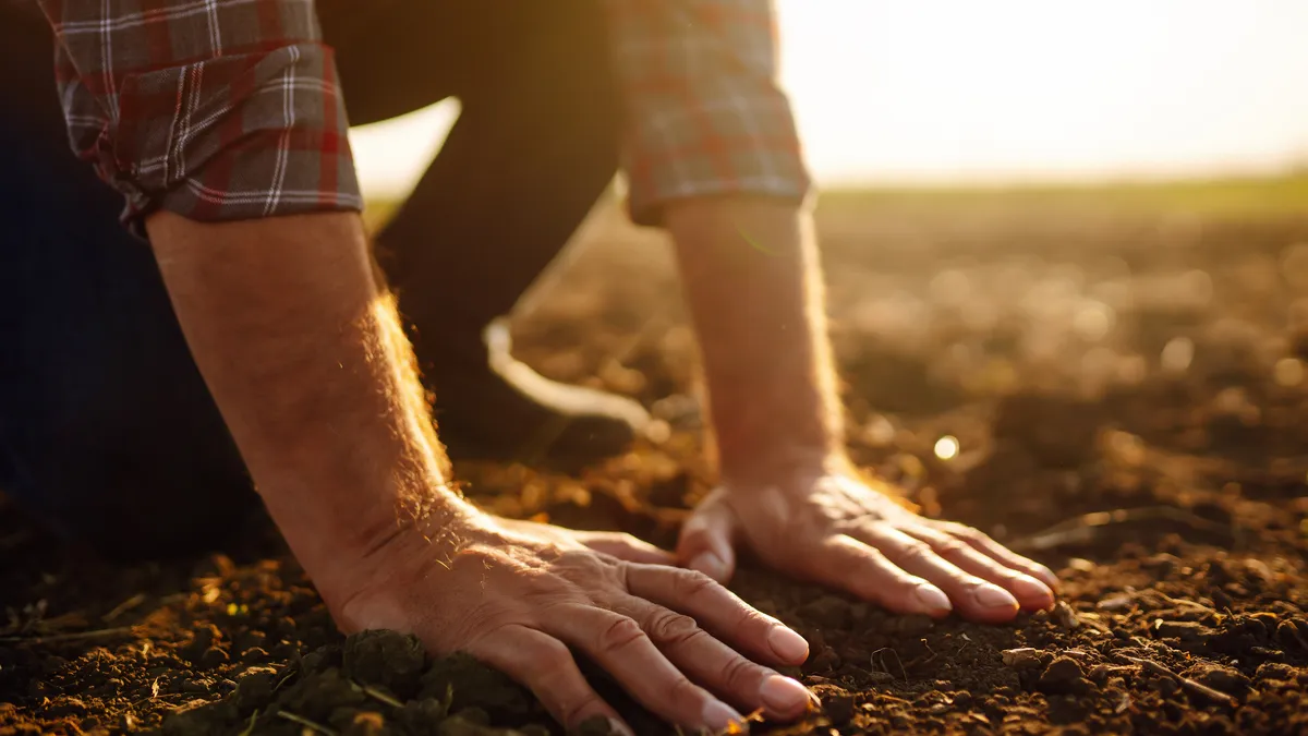 A farmer presses his hands into bare soil