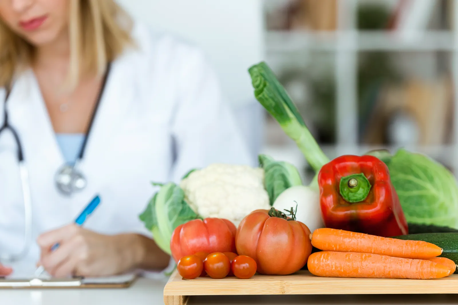 A nutritionist working at desk and writing medical records near fresh fruit.