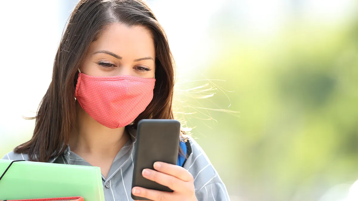 A college student with a pink face mask looking at ther phone.