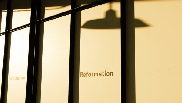 Black lines in a closeup of a store window, with the word "Reformation," and a slightly blurry shadow of a light fixture are bathed in yellow light.