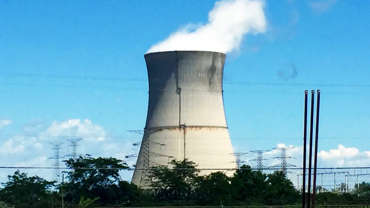 Steam rises from a large, concrete power plant cooling tower.