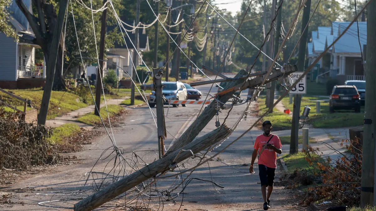 A man walks on a street with downed power lines.