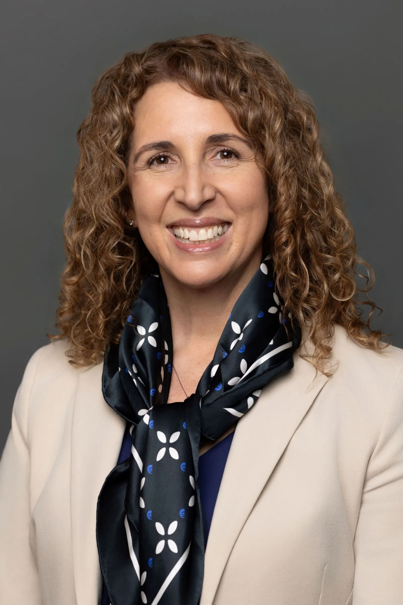A person wearing a blazer and scarf smiles for the camera.