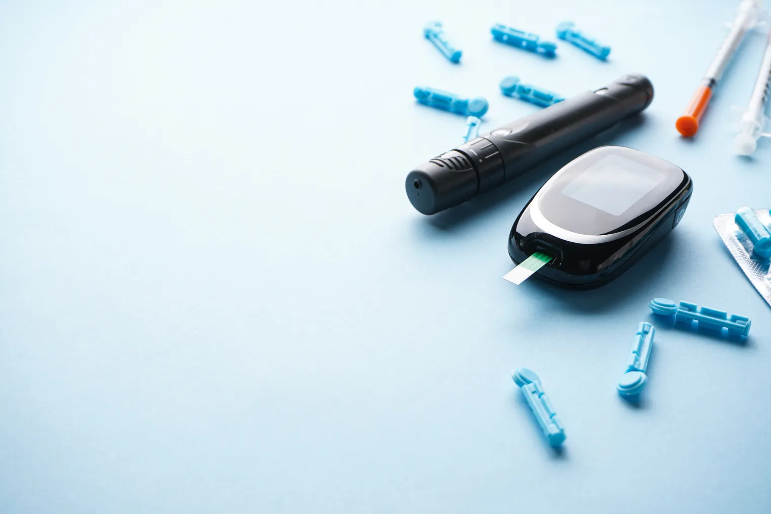 A glucometer, insulet pen and syringes on a blue background