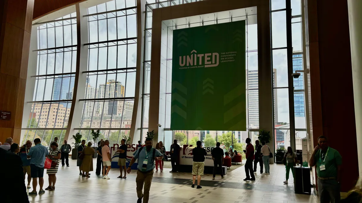 A large banner that says "UNITED" hangs inside in front of a large window. Outside the window are tall buildings. Inside people are walking around.