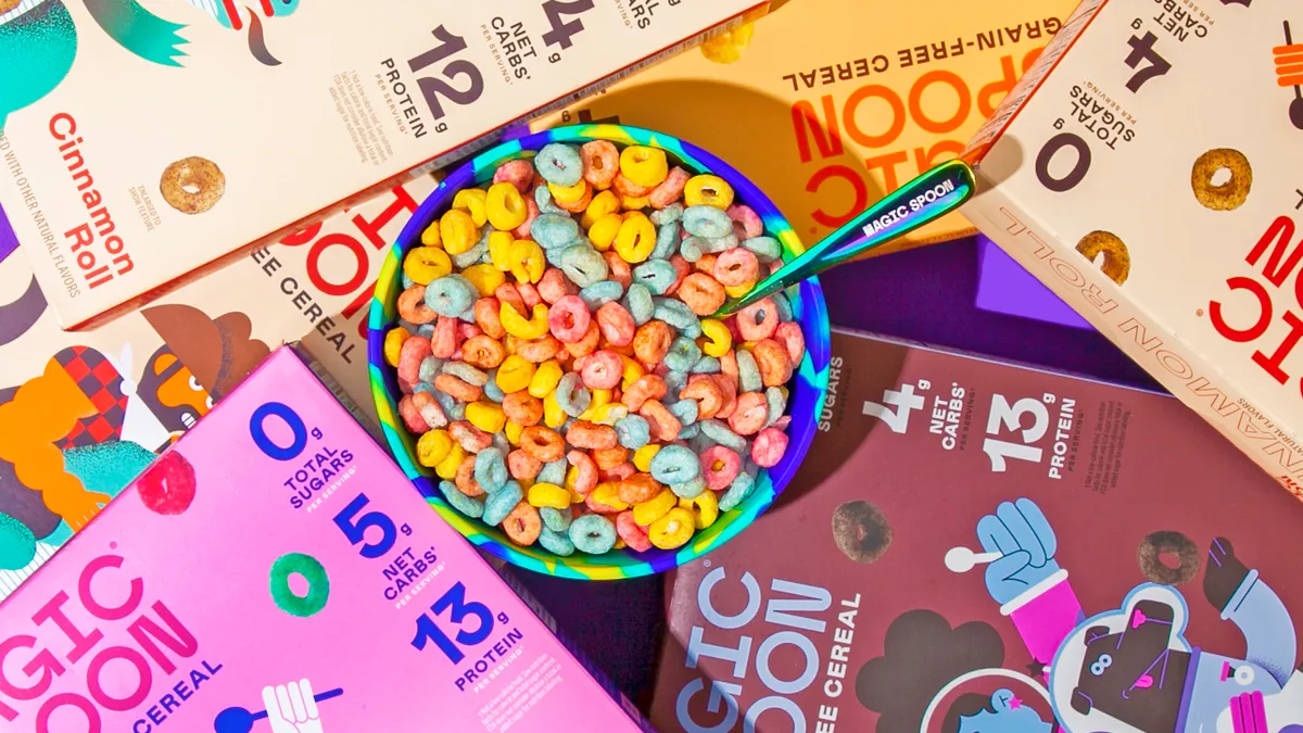 Boxes of several varieties of Magic Spoon cereal lay around a bowl of the multicolored Fruity variety.