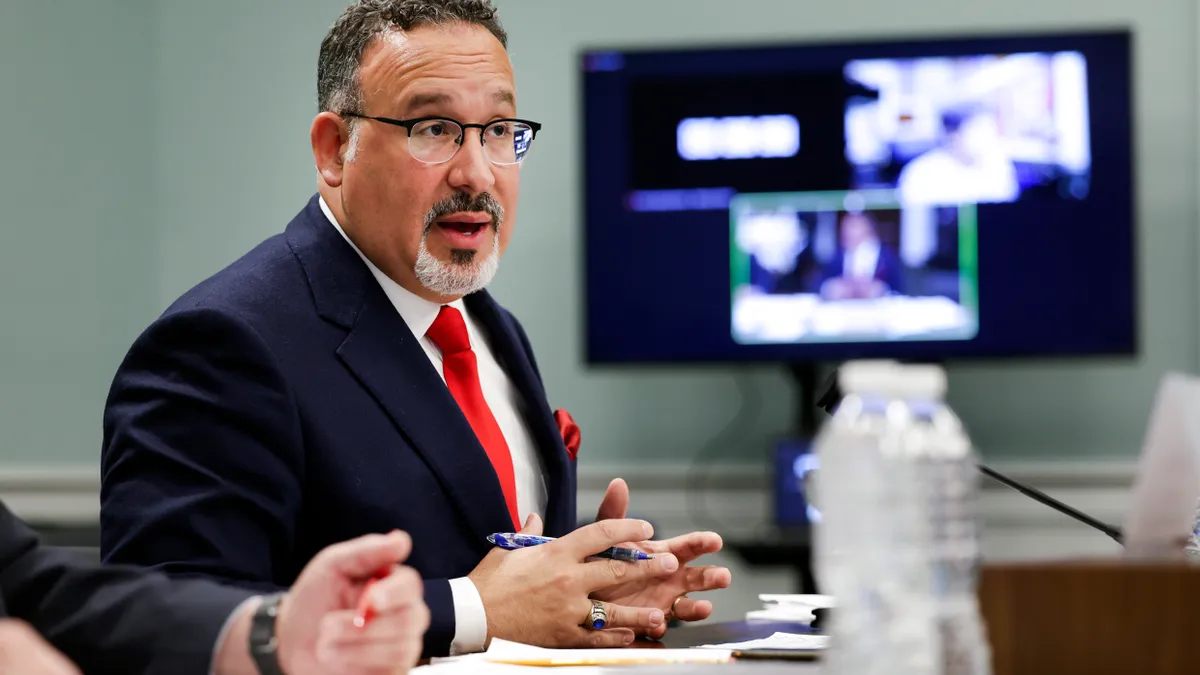 U.S. Secretary of Education Miguel Cardona sits at a table.