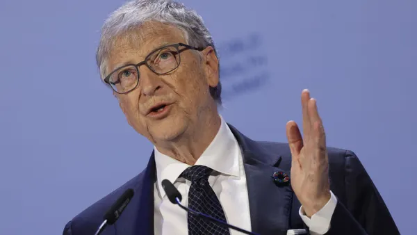 A person in a business suit speaks at a microphone.