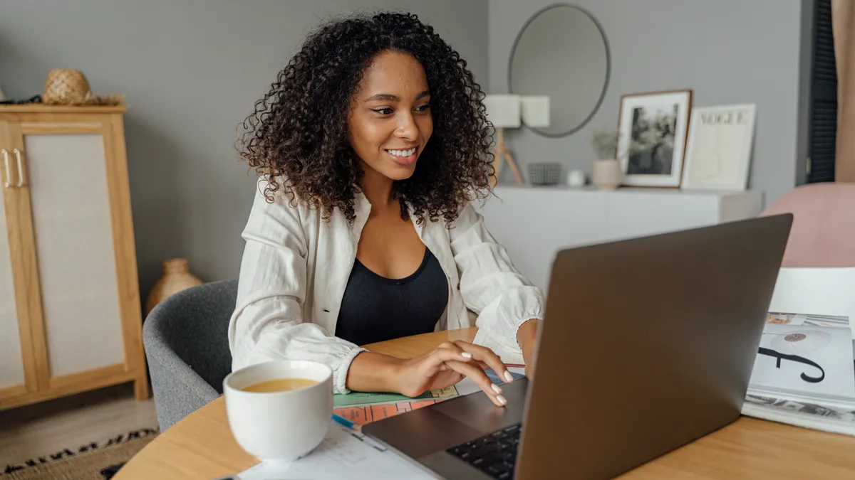 A Black person smiles, typing on a laptop at home