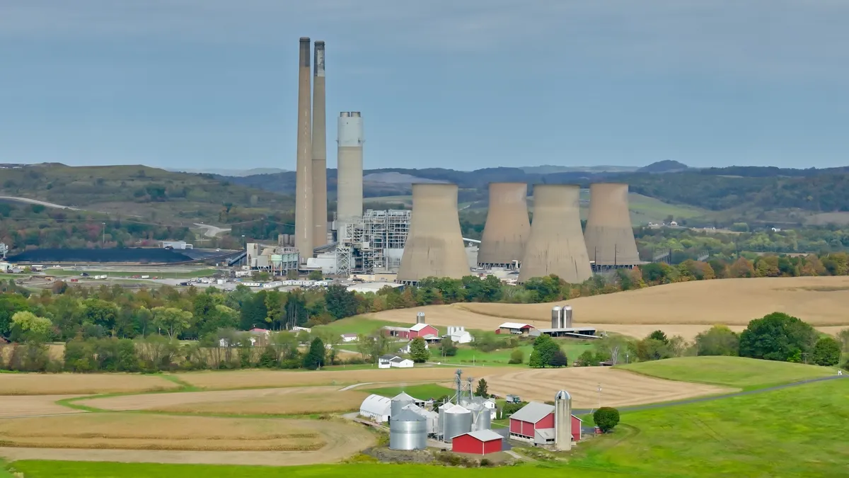 A power plant's smokestacks and cooling towers stand amid fields and woods.