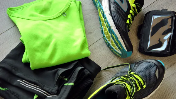 Bright neon green T-shirt sits folded on top a pair of black track pants on the floor next to a pair of sneakers.