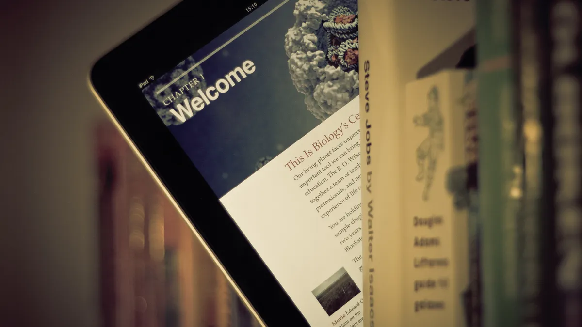 An iPad displaying a textbook peeks out from a library shelf of paper books