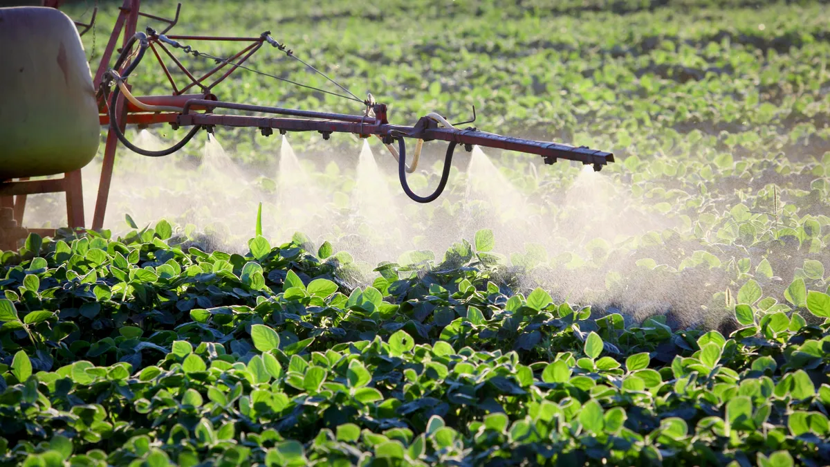 A herbicide sprayer is seen on a soybean field