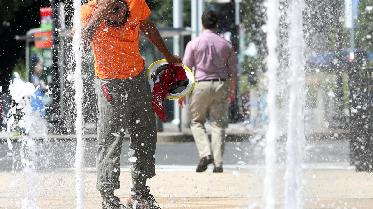 A construction worker out in the heat cools off in water fountains.