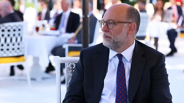 Russ Vought is shown looking to his right with other people seated behind him in the background.