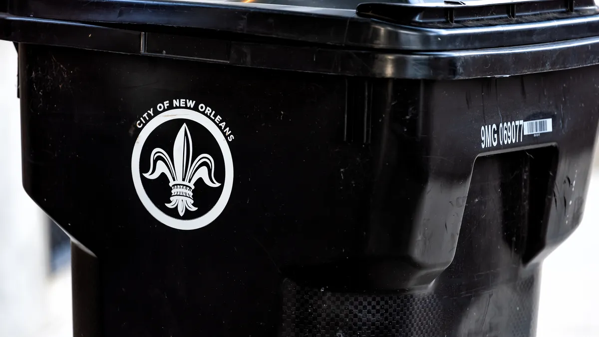 A close-up of a black trash bin with the City of New Orleans fleur de lis symbol