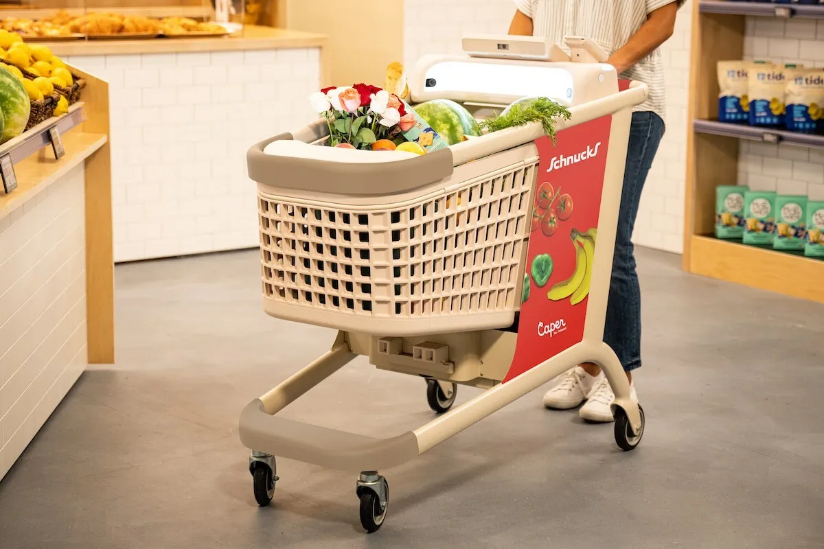 A shopper pushing a Schnucks-branded Caper Cart in a grocery store.