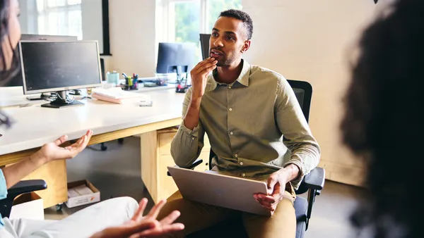 A person sitting down and talking with a coworker with their laptop in the their lap