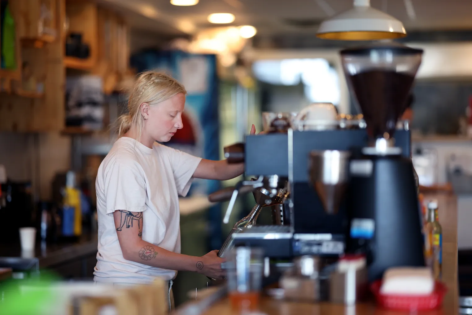 A person in a white t-shirt works behind the counter at a cafe.