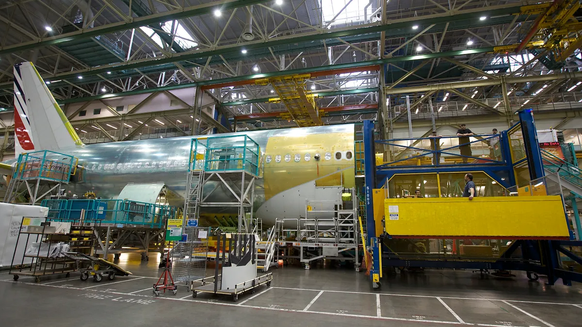 An aircraft being build inside of a facility, featuring half the body of an unfinished aircraft with workers standing by.