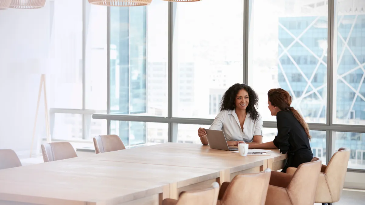 Two people sit and talk in a conference room.