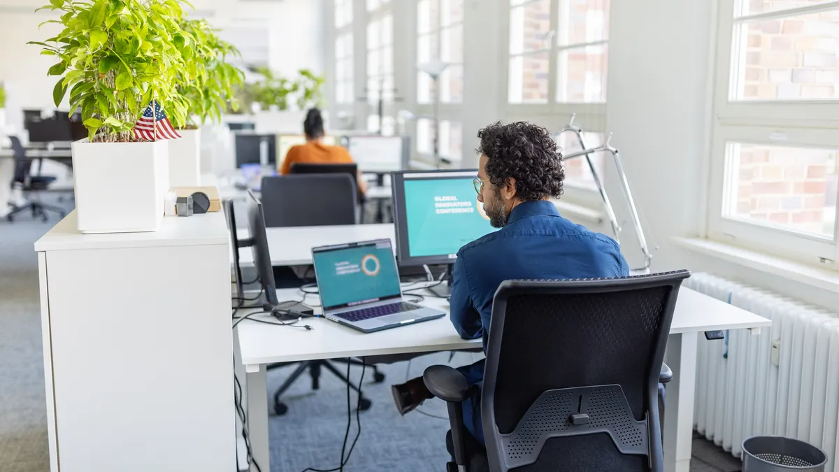 Person working on laptop and desktop computer at office.