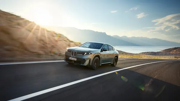 An all-electric BMW iX4 sedan traveling on a highway with a body of water in the background in a BMW media photo.