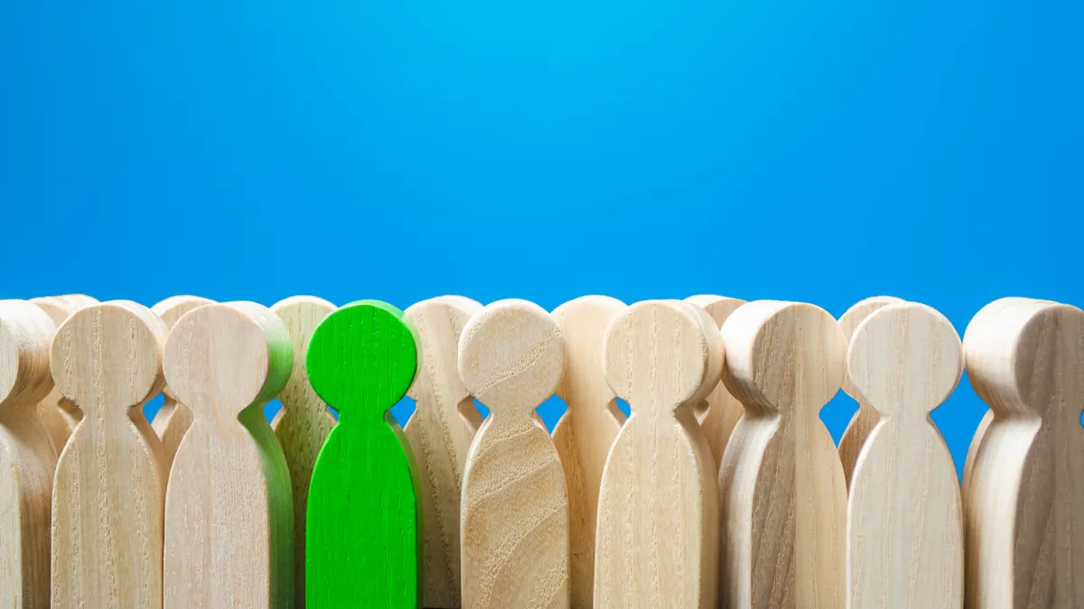 Green man figurine in a people crowd. Recruiting new workers, headhunters. Search for talented workers specialists. Stands out from crowd. Different, special. A talented and capable candidate.