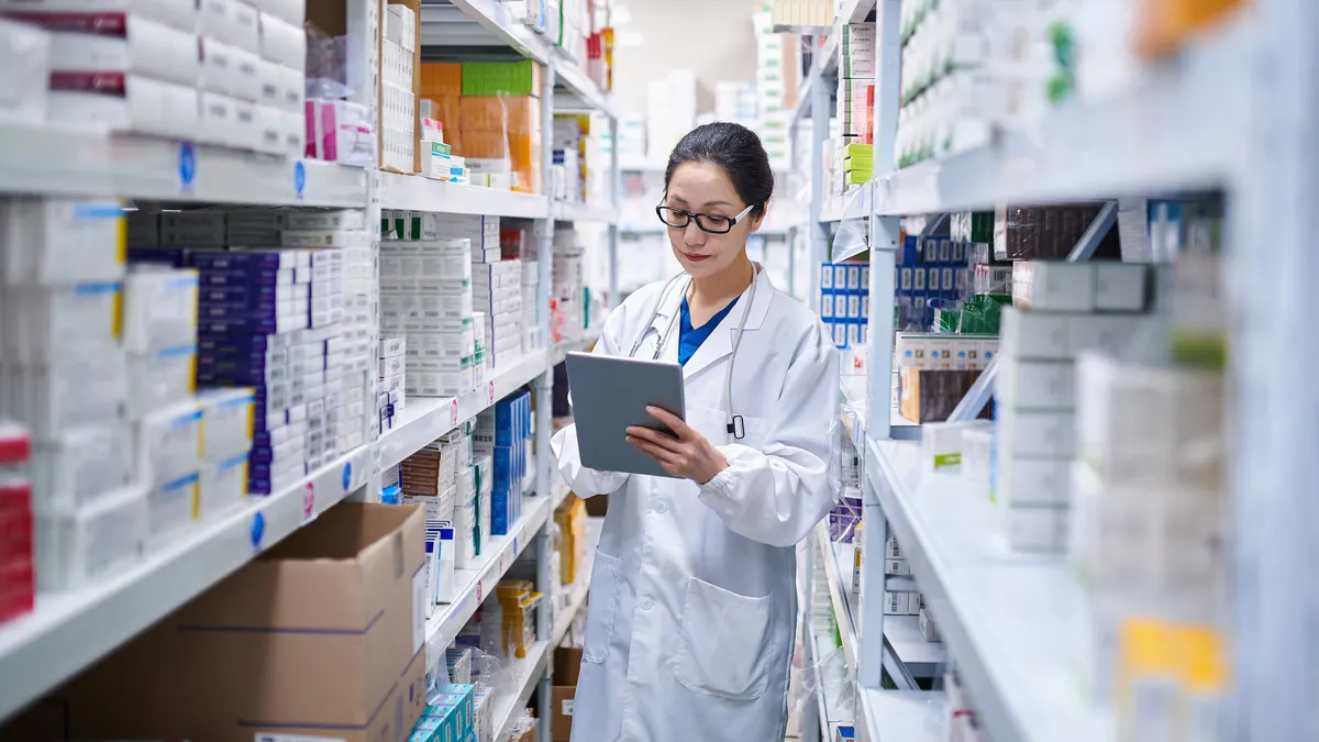 A pharmacist takes inventory of prescription drug cartons using a digital tablet.