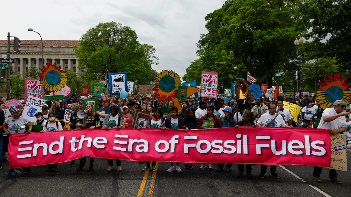 Activists participate in an Earth Day march with a sign that says "End the Era of Fossil Fuels"