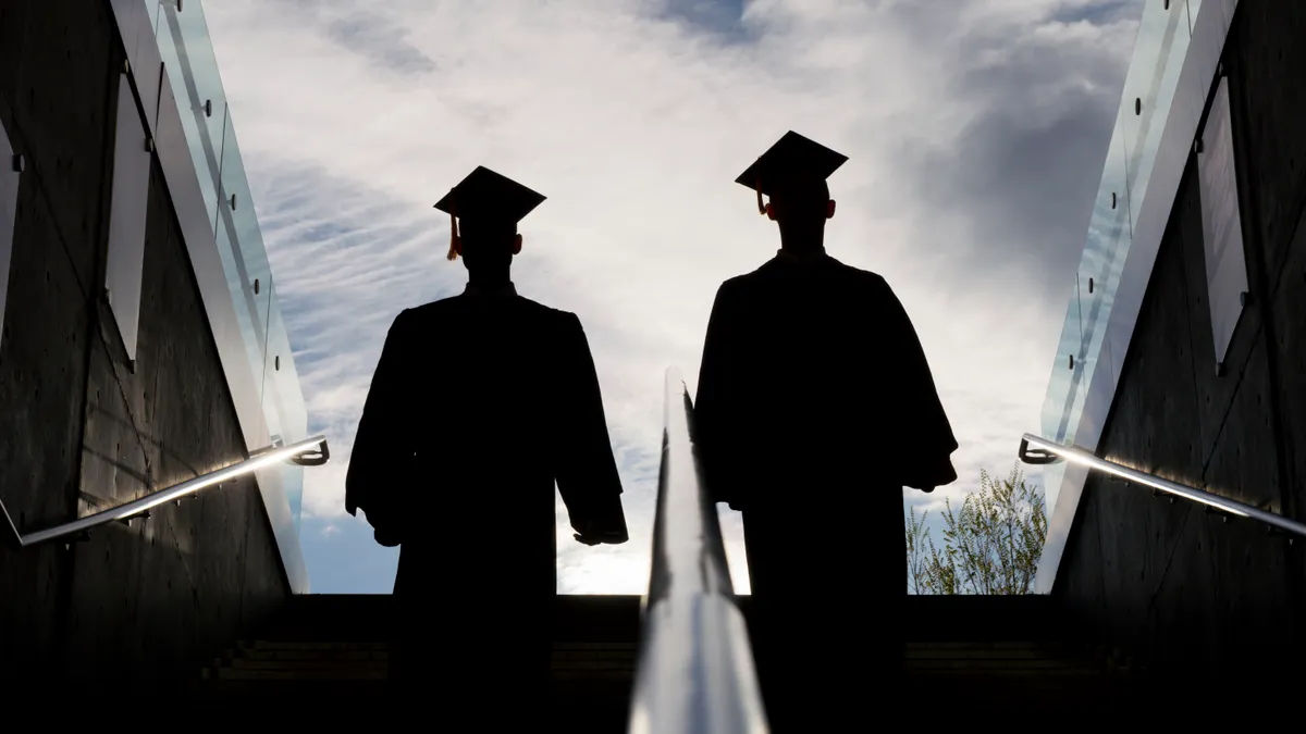 The silhouettes of two people standing on steps in caps and gowns, their entire figures are obscured.