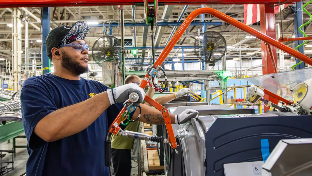 A worker builds an appliance on a factory floor.