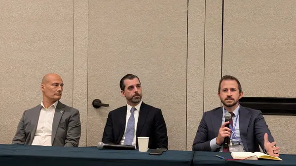 Three men sit behind a table in a conference ballroom