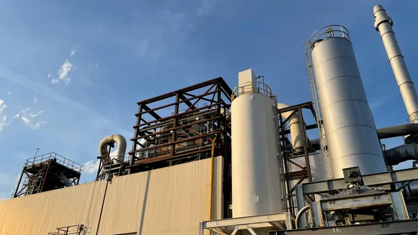 Exterior view looking up at the roof of an industrial facility with pipes, tanks and scaffolding.