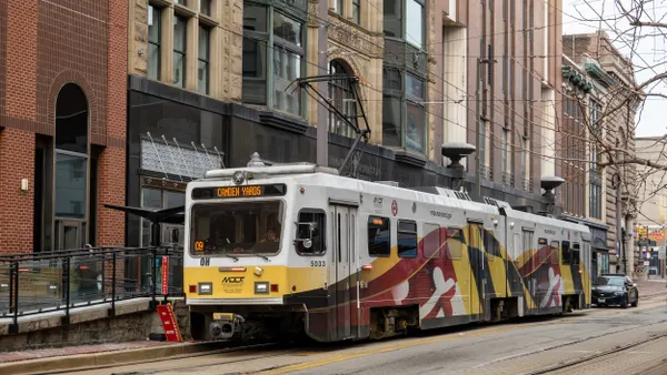 A 2-car tram under an electric wire on a street with buildings behind it.
