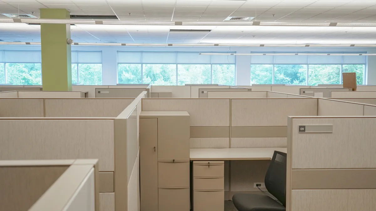 An office filled with cubicles and windows in the background.