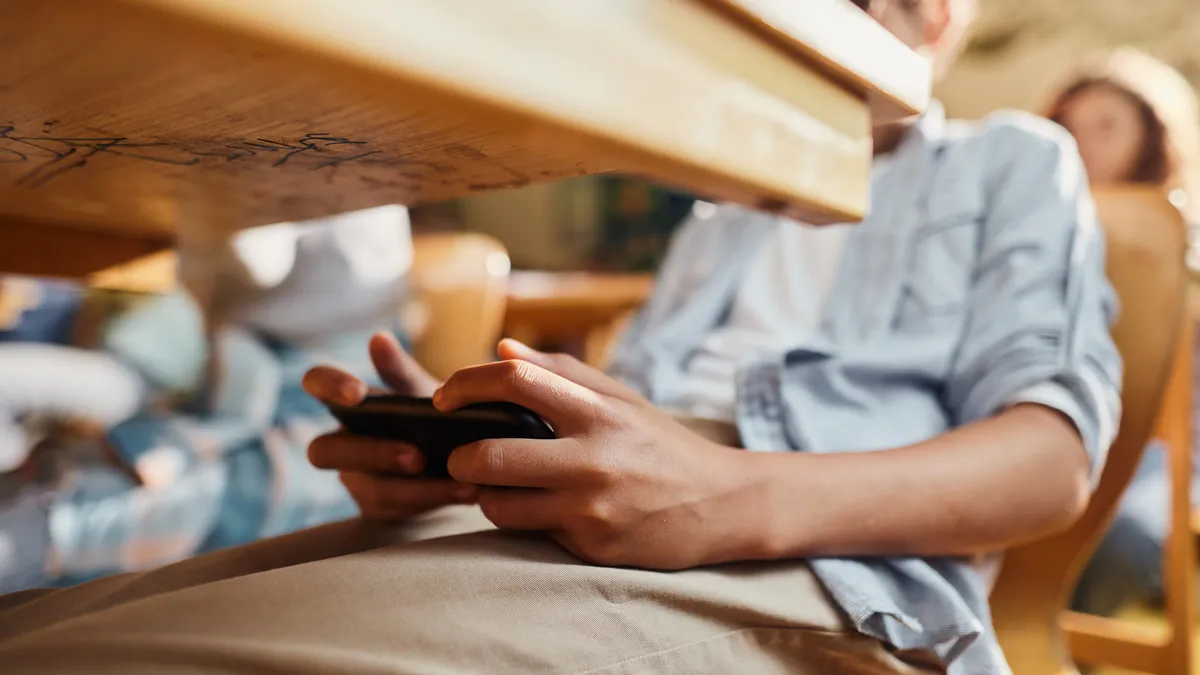 A close up of a student holding a cell phone under a desk in a classroom