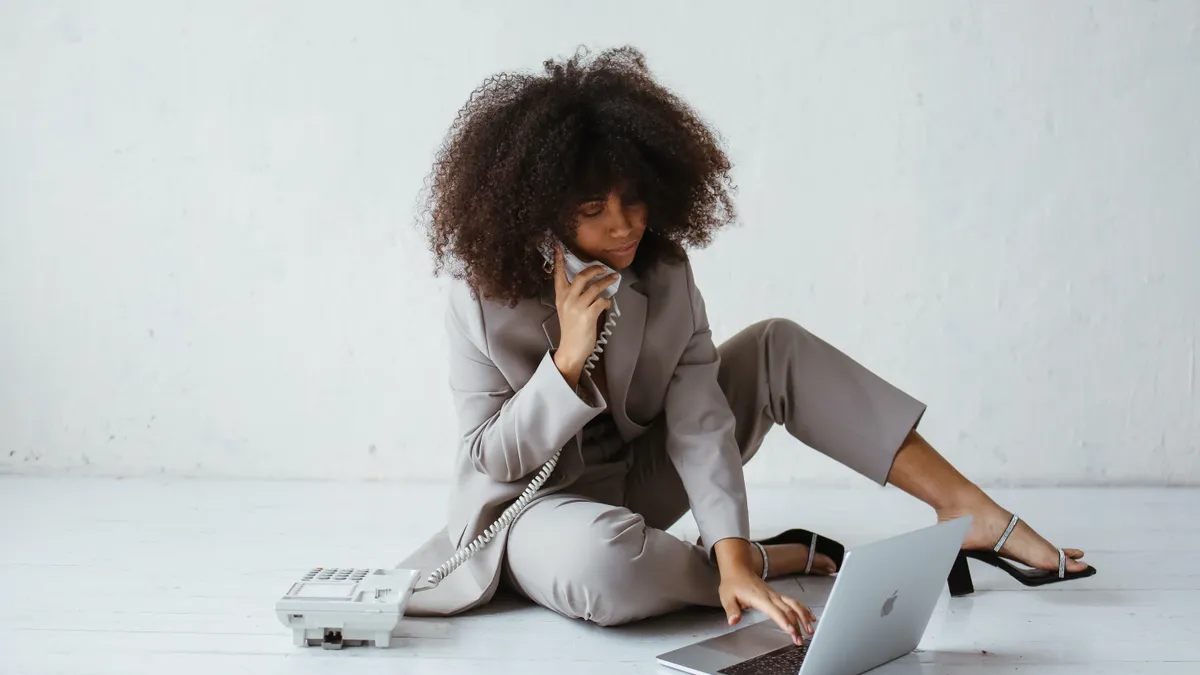 A Black businessperson types on a laptop, multi-tasking