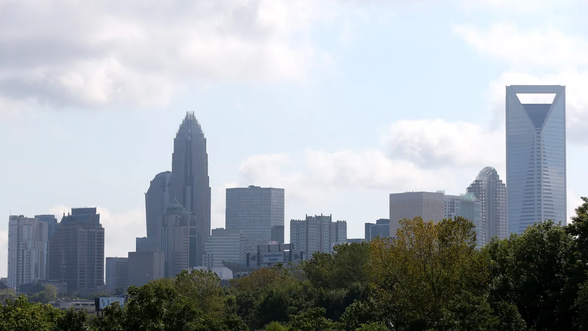 The Charlotte skyline rises behind a row of trees.