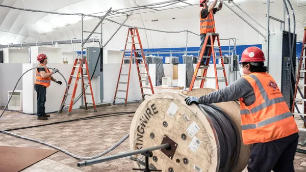 Construction workers build a structure while wearing masks.