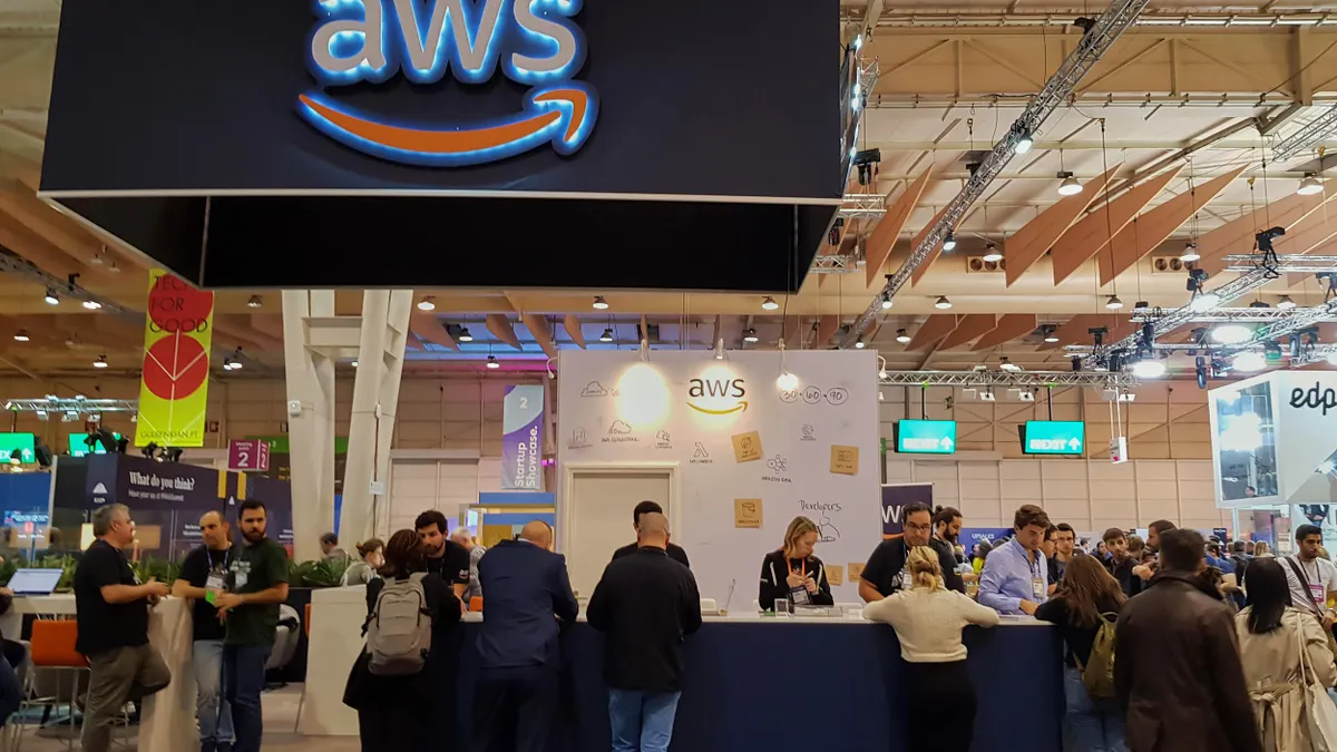An AWS logo is displayed above an exhibition stand, with attendees engaging in discussions and exploring the booth's offerings.