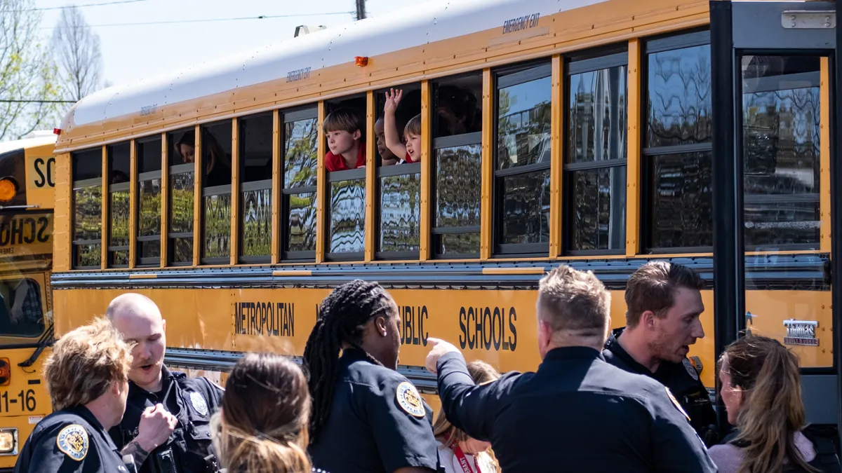 Children sit inside a bus looking out the window as police officers crowd around the bus doors