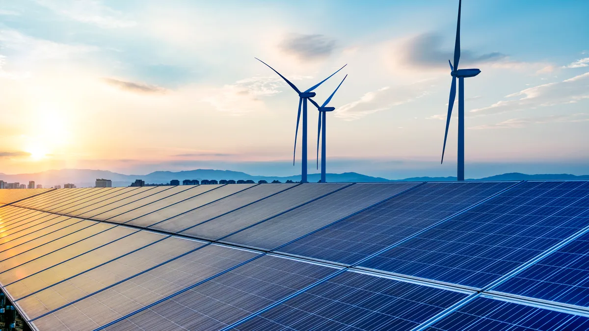 Wind turbines stand over an array of solar panels.