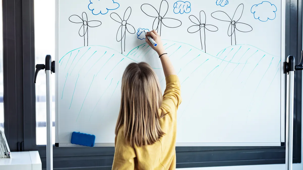 A student draws a windmill farm on a whiteboard.