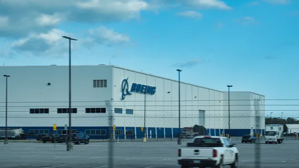 A white pickup truck driving in front of a beige building with the blue Boeing logo.